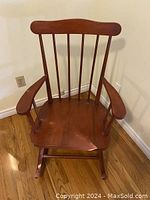 Maple rocking chair front view without cushions, showing spindle back and wide armrests.