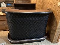 Front view of a vintage mid-century modern bar cabinet with black tufted leather front and black leather trim with wooden foot rail base.