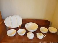 Serving set including platter, large bowl, small bowls, sugar bowl, and creamer arranged on wooden shelf.