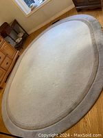 Oval neutral carpet rug placed on wooden floor, showing overall design and shape.