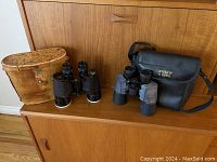Overview of both pairs of binoculars and their respective cases placed on a wooden surface