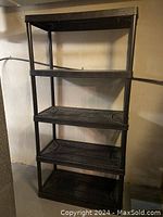 Full view of a black plastic shelving unit with five shelves against a wall.