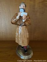 Front view of Royal Doulton The Detective figurine showing the detective holding a magnifying glass and a notepad, with a pipe in his mouth and detailed trench coat.