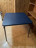 Top view of square navy lace folding card table with metal legs.