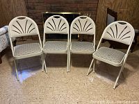 Four white metal Samsonite folding chairs with cushioned seats, one chair showing a small fabric repair on the seat.