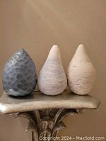 Three signed decorative pottery pieces with teardrop shape and different textured finishes placed on a decorative stand.