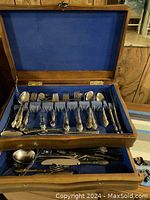 Open wooden case displaying cutlery arranged neatly in blue felt compartments