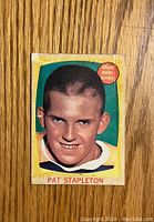 Front view of 1961-62 Topps Pat Stapleton hockey card showing player portrait with green and yellow background, Bruins badge at top right corner.
