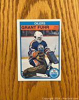 Front of 1981-82 O-Pee-Chee Grant Fuhr hockey rookie card showing player in goalie stance in Oilers uniform with card number 105.