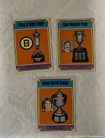 Front of three 1974-75 O-Pee-Chee hockey cards showing Prince of Wales Trophy (Boston Bruins), Calder Memorial Trophy (Denis Potvin), and James Norris Trophy (Bobby Orr).