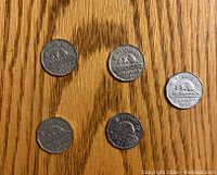 Five Canadian 5 cent nickels arranged on a wooden surface, showing the reverse side with the beaver and date: 1948, 1949, 1950, 1951, 1952.