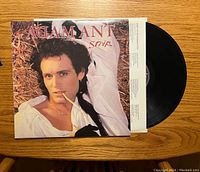 Front view of the Adam Ant 'Strip' vinyl record partially pulled out of its album cover, showing Adam Ant lying with a piece of straw in his mouth.
