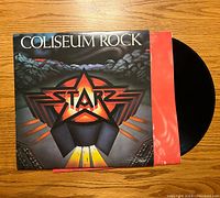 Front cover of the vinyl album 'Coliseum Rock' by Starz showing artwork with star logo and rocky background. Red inner sleeve partially visible with black vinyl disc.