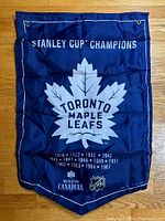 Blue Toronto Maple Leafs Stanley Cup Champions banner with white print and metal grommets shown flat on wood floor