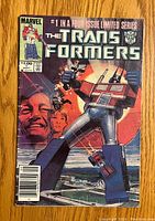 Front cover of The Transformers comic issue #1 showing Optimus Prime and background characters with some signs of wear and creasing on edges and spine.