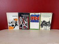 Front view of four 1960s dystopian fiction paperback novels against red background, showing Animal Farm, Brave New World, 1984, and Lord of the Flies