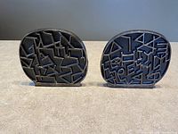 Front view of two black metal bookends with abstract raised Hebrew alphabet patterns.