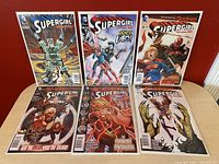 Seven comic books laid out on a table showing front cover art from various SuperGirl The New 52 issues including #26, #27, #30, #31, #33 (two copies), and #35. Comics are in protective bags and backed with boards.