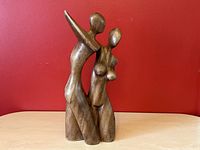 Front angled view of the wood sculpture showing the abstract cubism-style couple with polished wood surfaces against a red background.