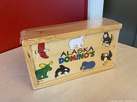 Front view of the wooden Alaska Dominos box showing colorful wildlife and sealife illustrations, shrink-wrapped in cellophane.