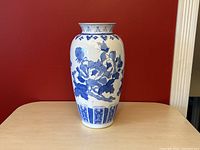 Full front view of the slightly tapered vase, showing the detailed blue peony and butterfly design on white background against red wall.