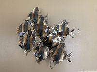 Metal fish wall hanging art, showing front view of six fish arranged together, mounted on a beige wall.