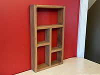 Wooden Mid Century Modern floating display shelf photographed against a red wall, placed on a light wood surface showing front and side views.