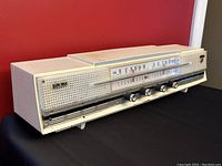 Front and angled view of retro white plastic Rincan radio showing tuning scale, control knobs, and speaker grille pattern.