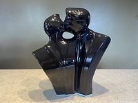 Front view of glossy black ceramic sculpture showing man and woman kissing, detailed reflection and silhouette.
