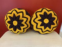 Pair of round vintage crochet pillows with yellow and brown starflower design against a red background.