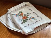Folded vintage cross stitch tablecloth showing floral pattern and border