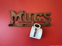 Wooden wall hanging mug rack showing the 'Mother's Mug Made in England' ceramic mug hanging on the right peg.