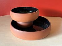 Photo showing stacked terracotta chip and dip bowls with black glazed interior and matte terracotta exterior.