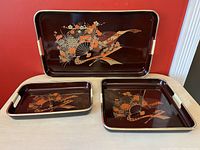 Three vintage Japanese nesting trays shown stacked and displayed, dark lacquer finish with gold trim and floral fan design
