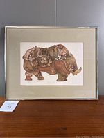 Full front view of framed rhinoceros etching by David Campbell displayed against a gray wall.