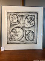 Front view of framed pen and ink drawing showing four abstract faces and silver frame