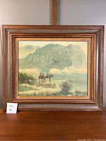 Front view of framed oil painting showing a Native American scene with riders on horseback and mountainous landscape.