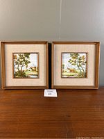 Two framed Castelli tile paintings side by side showing landscape scenes with trees and rural houses in wooden frames with beige matting.