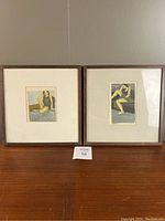 Pair of framed watercolor portrait paintings by Susan Sarner, showing full view of the two artworks side by side on a wooden surface, with visible slight shifting inside frames.