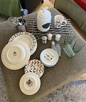 Photo showing plates with various motifs including Emma Bridgewater dinner plates, salad plates, wine motif plates, chicken biscuit jar, salt and pepper shakers, glass bottles, green glasses, cooling rack