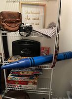 Wide view of shelf with leather pocketbook, framed quote, camera, pom-pom hat, crayon bank, and stack of board games.