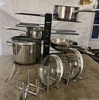 Full view of stainless steel cookware including pots, frying pans with lids and IKEA metal organizers for storage.