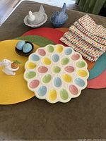 Full lot view showing egg platter, chicken shakers, placemats, napkins, egg shakers, and bunny figurine on tabletop