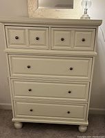 Front view of Pier 1 Ashworth 5 drawer chest showing off-white color, drawer configuration with round black knobs and ball feet.