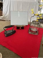 Photo showing antique flat iron, Buddha Board, and flower vase on a red cloth.