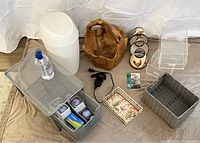 Complete lot displayed on beige surface with white backdrop, showing wooden bucket, metal slide-out storage, towel holder, trash can, hand sanitizer, baskets, and other items.