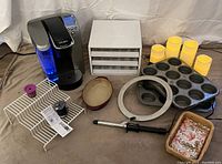 Full lot showing all items including Keurig coffee maker, cupcake tins, electric candles, spice drawer organizer, baking dish, curling iron, and bathroom basket with towels