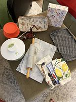 Full view of lot items including marble rolling pin, salad spinner, dish towels, baking sheet, cooling racks, apple corer/slicer, basket, and cereal tin