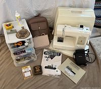 Full view of Kenmore sewing machine with lid, storage box with sewing notions, two bags, Hogwarts playing cards, and antique sequin bag.