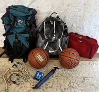 Full lot laid out including two backpacks, two basketballs, carabiners, bungee cords, hand pump, and needle pack.